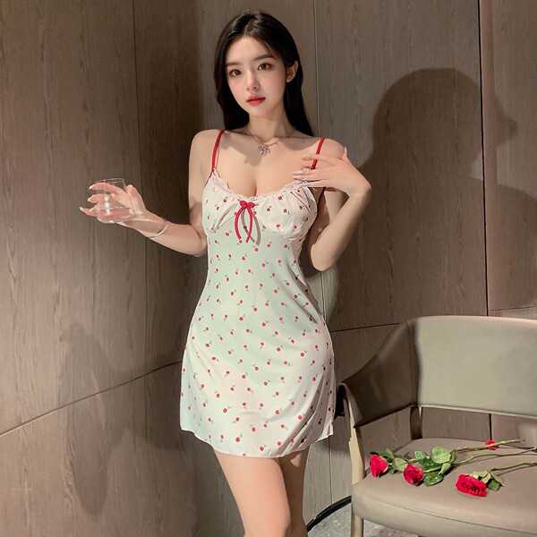Woman wearing a light green cherry-print babydoll sleep set with red straps and bow, holding a glass; includes built-in pads ...
