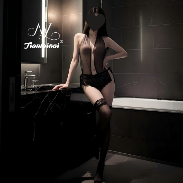 Woman wearing sheer black seductive deep-v lace bodysuit with cross-straps and thigh-high stockings in a modern bathroom.