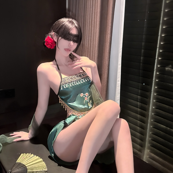 A woman poses elegantly wearing a green exotic-style bralette with floral embroidery, paired with sheer fabric accents. the d...