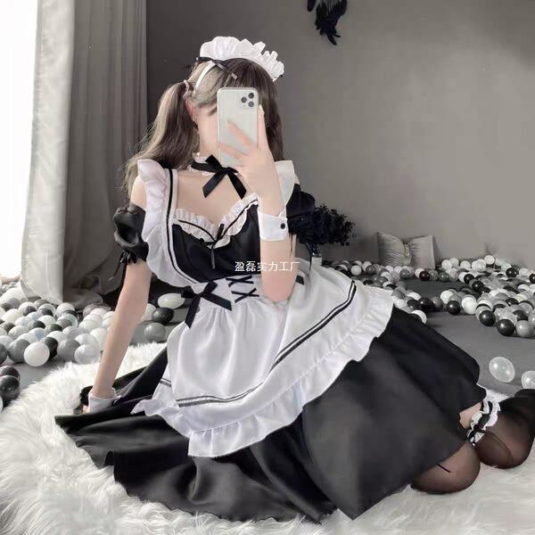 A woman wearing a black and white maid costume, featuring ruffles and bows, poses indoors with balloons scattered around. the...