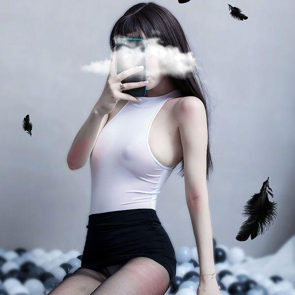 A woman poses with a smartphone, partially obscuring her face as feathers float around her. she wears a white bodysuit paired...