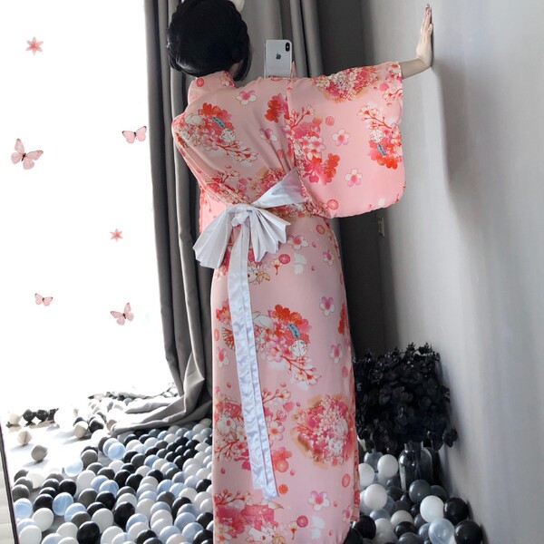 A woman wears a pink floral japanese kimono-style lingerie set, featuring long sleeves and a bow tie, perfect for elegant nig...