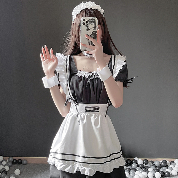 A woman wearing a black and white maid costume, featuring ruffled sleeves, a corseted apron, and a headband, posing with a ph...