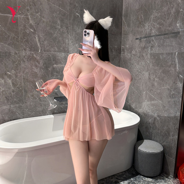 A woman poses in a bathroom wearing a pink sheer lace sleep dress with an open-crotch design, holding a glass of champagne wh...