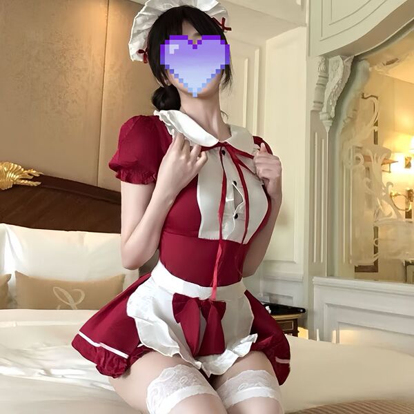 A person wearing a red and white maid costume set, featuring a ruffled dress, apron, and stockings, sitting on a bed with a h...