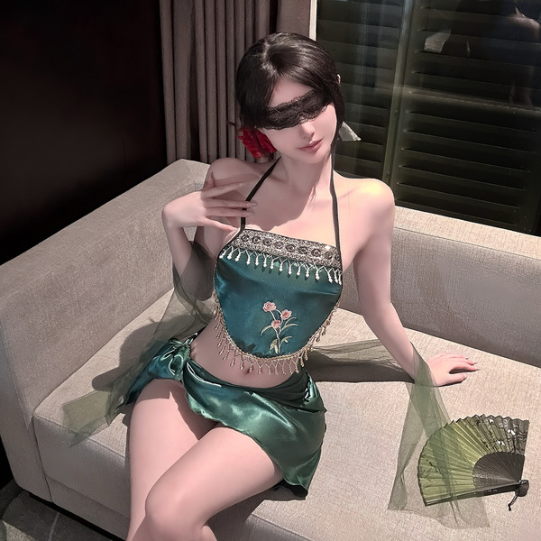 A woman poses elegantly on a couch wearing a luxurious green exotic strapless lingerie set, featuring intricate embroidery an...