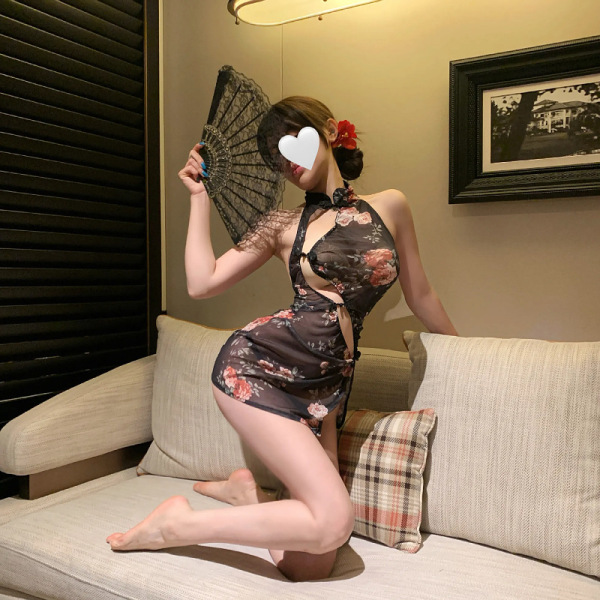 Woman posing in a sheer vintage qipao dress with lace trim and high slit, holding a fan on a sofa.
