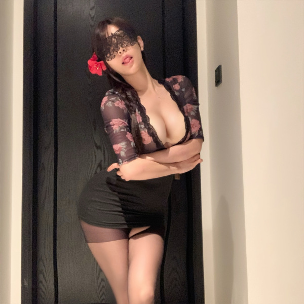 Woman in black floral lingerie set with bodycon skirt, lace mask, and red flower hair accessory.
