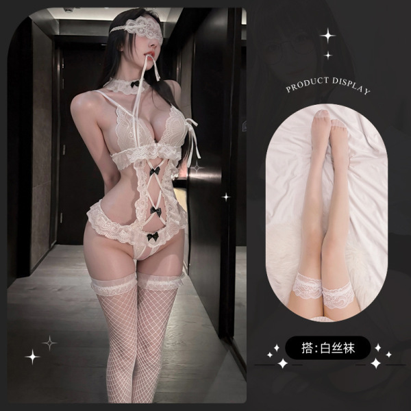 Woman modeling white lace lingerie set with bondage-inspired straps, garter belt, and fishnet stockings in hallway.