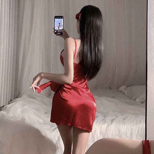 A woman poses in a red satin slip dress, capturing herself in the mirror. the sexy, adjustable-strap design features romantic...
