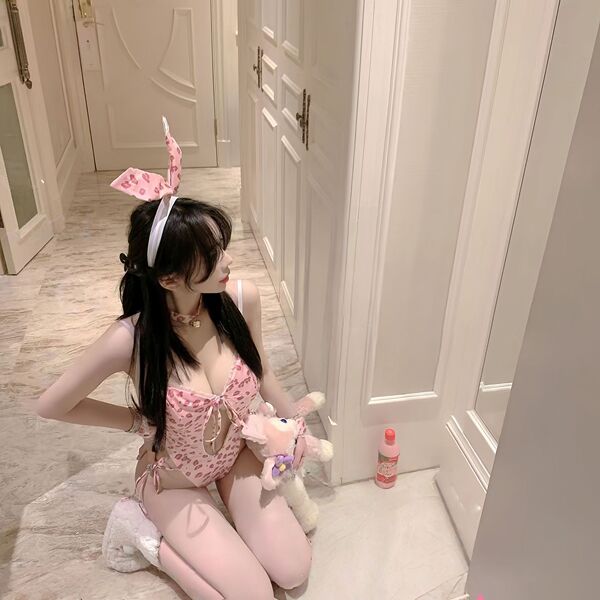 Woman in pink rabbit girl lingerie set with bunny ears, holding plush toy, kneeling on floor for role play.