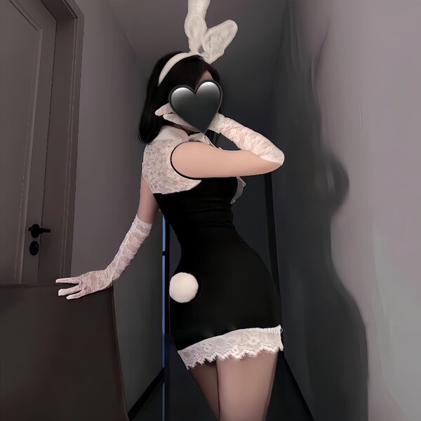 Woman in black bodycon dress with white lace trim, bunny ears, and gloves posing seductively in a doorway.