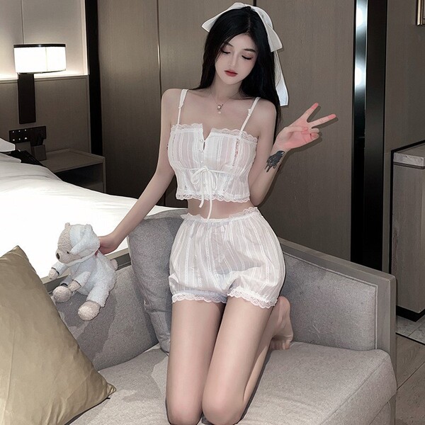 Woman in white sheer lingerie set with lace trim, bow headband, and peace sign gesture on sofa.