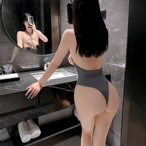 Woman in gray lace bodysuit posing in bathroom mirror, showcasing open-crotch design and sleek silhouette for seductive sleep...