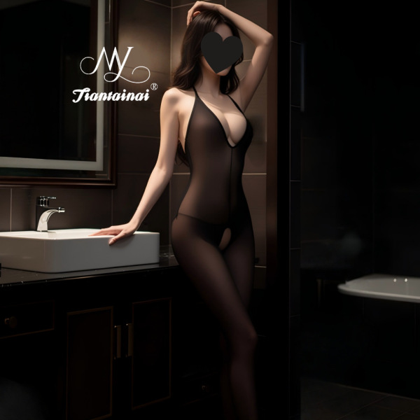 Woman in black low-back halter bodysuit with sheer stockings and open-crotch design, posing seductively in a modern bathroom.