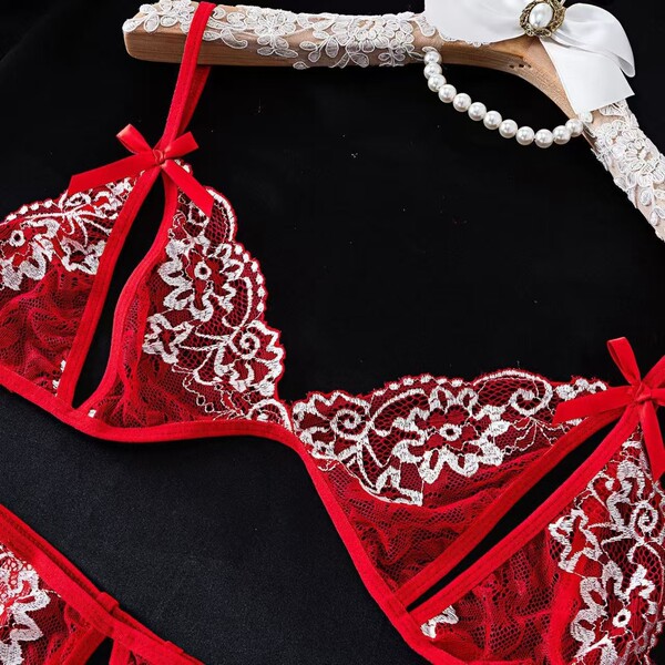 Red lace lingerie set with floral embroidery and bow details, displayed on a hanger with pearls.