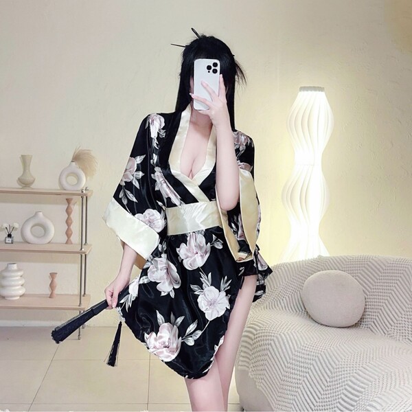 A woman poses in a japanese kimono lingerie set featuring a floral print and dramatic sleeves, holding a fan against a cozy r...
