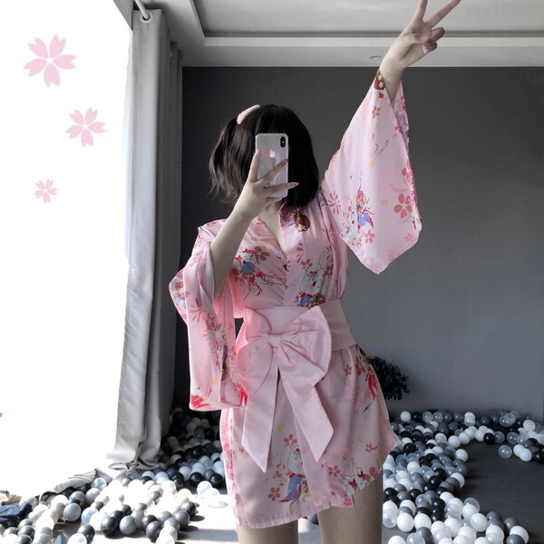 A woman poses with a phone, wearing a pink floral japanese-style kimono robe set. the ensemble features lace details and a bo...