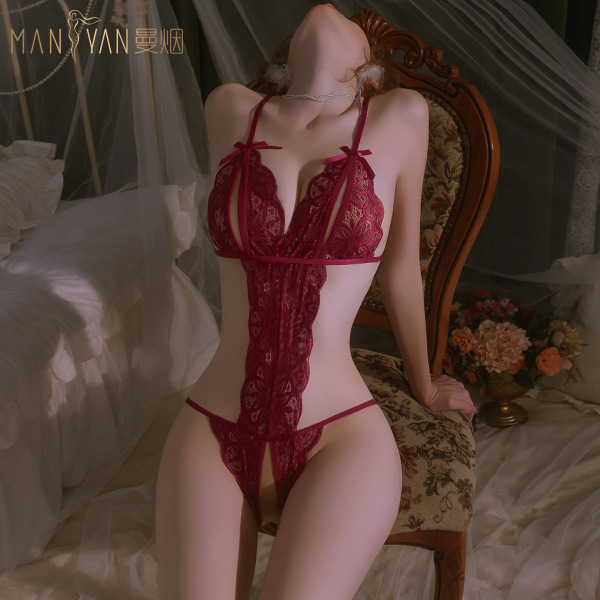 Woman wearing mannyan red lace open-crotch bodysuit with sheer mesh, posing on ornate chair in romantic bedroom setting.