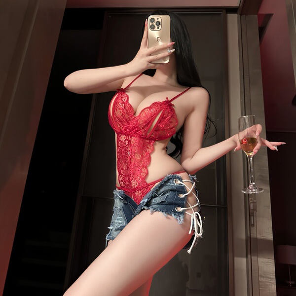 Woman in red lace bodysuit with denim shorts, holding wine glass and phone. night-silk sensual open-crotch lace bodysuit set.