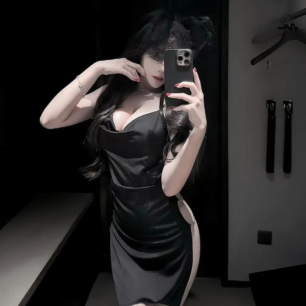 Woman in black satin qqny pure & sexy knotted neckline sleep dress, body-con fit, posing with phone mirror selfie.