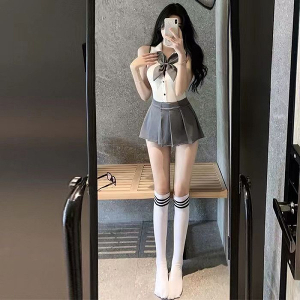 A woman poses in a mirror wearing a cute japanese school uniform style jumpsuit with a bow tie, knee-high socks, and white st...