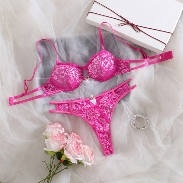 Pink lace bra and thong set with floral pattern, displayed on white fabric with roses and gift box.