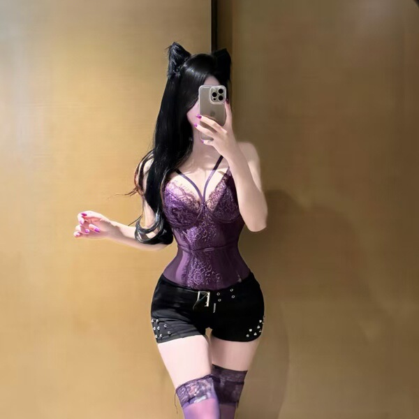 Woman wearing purple lace lingerie set with black shorts and thigh-high stockings, taking a mirror selfie.
