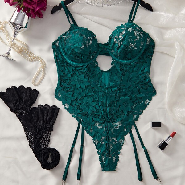 Emerald green lace bodysuit with open-crotch design, paired with black fishnet gloves, pearls, and lipstick on white fabric.