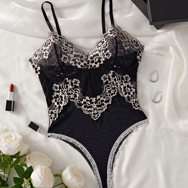 Black lace mesh bodysuit with floral details, styled as sensual sleepwear lingerie for women, displayed on white silk with ro...