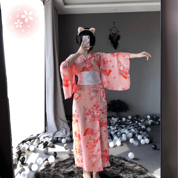 A woman poses in a mirror wearing a pink floral japanese kimono-style cat girl lingerie set, featuring elegant long sheer sle...
