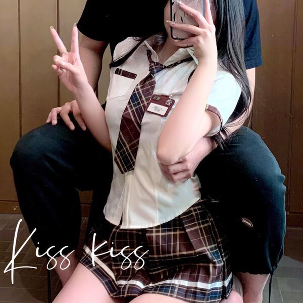 A person wearing a schoolgirl uniform with a plaid skirt and tie, posing playfully while holding a phone. the outfit features...