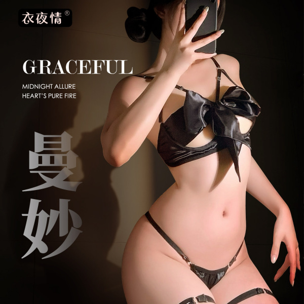 Woman modeling black satin bow-tie bralette and thong set, elegant erotic lingerie for adults.