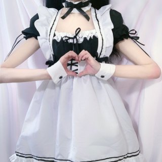 A person wearing a japanese-style black and white maid dress featuring lace trim and bows, making a heart shape with their ha...