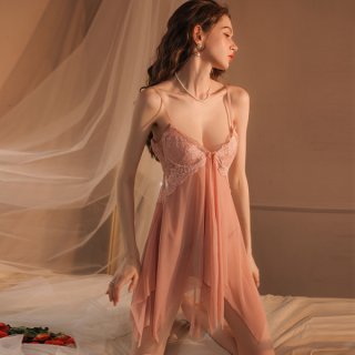 Woman in soft pink qqny lingerie set with lace bra and flowing robe, posing on bed with romantic lighting.