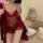 Woman wearing red sheer lingerie sleep set with matching robe, sitting on couch beside plush bunny and gift items.