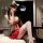 Woman modeling red pleated mini skirt set with white lace bra, cat ears, and thigh-high stockings on bed.