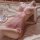 Woman in pink lace sleep dress with push-up cami, wire-free design, body-conscious fit, elegant trim on bed.