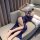 Woman lounging on sofa in blue lace lingerie set with feather fan, featuring modest straps and elegant nightwear design.