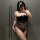 Woman wearing black lace lingerie set with fishnet stockings, posing in front of a mirror.