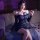 Woman in navy lace bodycon skirt set with sheer sleeves, posing on bed with rose petals for date night.