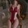 Woman wearing mannyan red lace open-crotch bodysuit with sheer mesh, posing on ornate chair in romantic bedroom setting.
