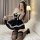 A woman poses on a bed wearing a black maid costume sleepwear set, featuring lace details, a bow tie, and thigh-high stocking...