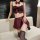 Woman modeling burgundy pure & playful lingerie set with bow details, mini skirt, and thigh-highs on beige couch.