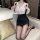Woman wearing white blouse, black skirt, and stockings in hotel room.