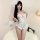 Woman modeling white lace open-crotch bodysuit with sheer floral pattern, ruffled hem, and matching feathered purse.