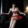 Woman in red pleated skirt set with lace top and bell choker, seated on black leather couch.