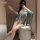 A woman poses with a mirror, wearing a sheer, teal chinese-inspired sensual outfit featuring a hanfu-style bustier dress. the...
