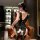 A woman sits on a leather chair wearing a black lace bodysuit with a pearl-embellished backless design and a decorative bow d...