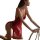 Woman in red lace babydoll sleep dress with sheer mesh and side slit, kneeling beside chair—romantic lingerie set.